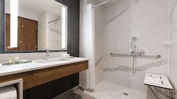 A modern bathroom with a marble shower, a wooden vanity, and a large mirror.