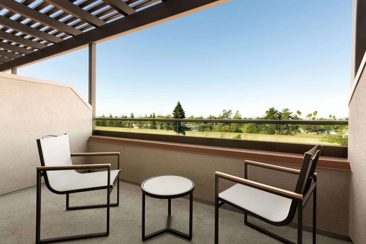 A balcony with two chairs and a small table, offering a view of a green landscape and distant buildings.