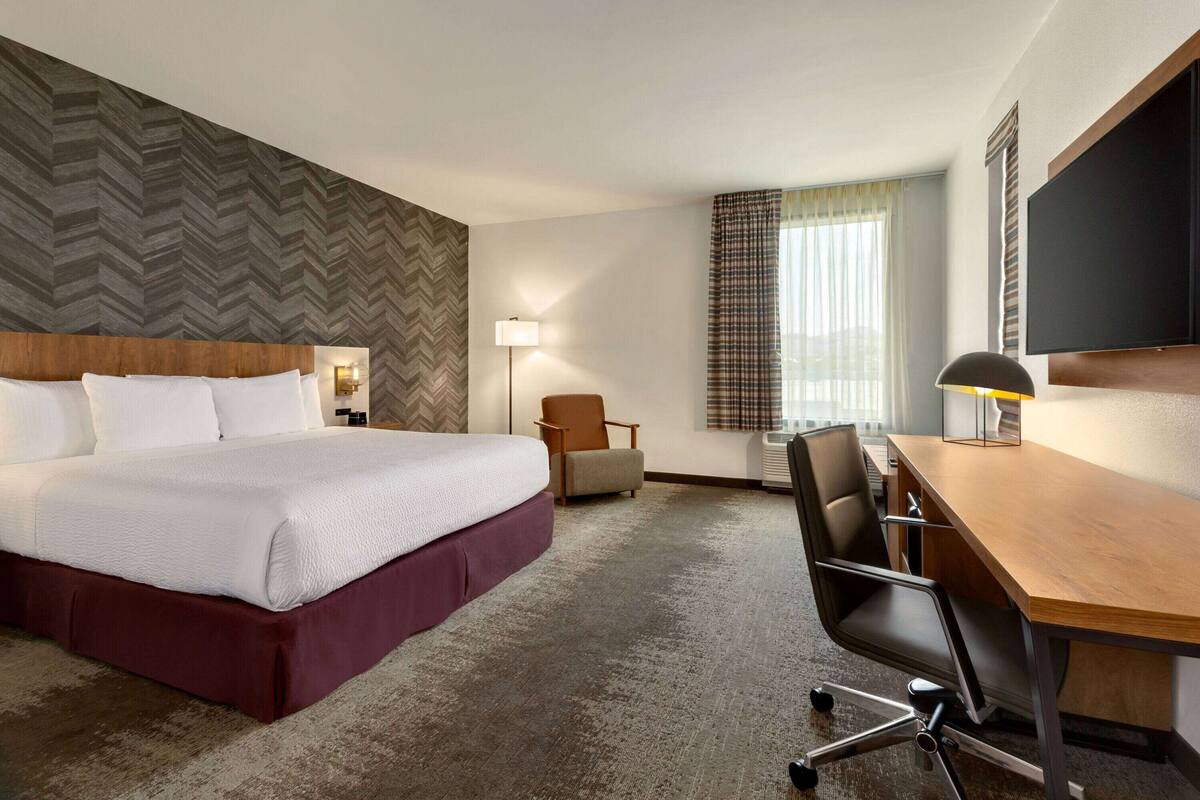 A hotel room with a large bed, a desk, a chair, a lamp, and a television.