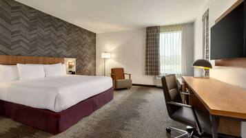 A hotel room with a large bed, a desk, a chair, a lamp, and a television.