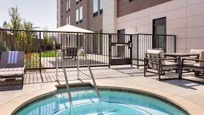 A swimming pool with a metal ladder, surrounded by a fence, and outdoor seating with tables and chairs.