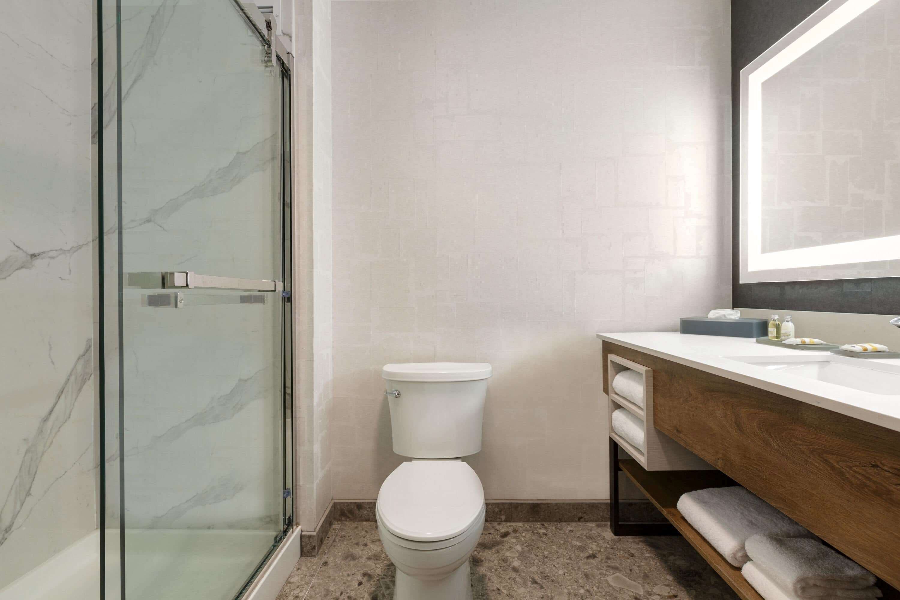 Une salle de bain moderne avec une douche à parois de verre, des toilettes blanches et un meuble-lavabo doté d’un miroir et d’un porte-serviettes.