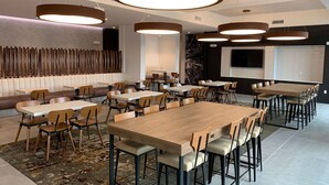 A modern dining area with wooden tables and chairs, a patterned rug, and pendant lighting.