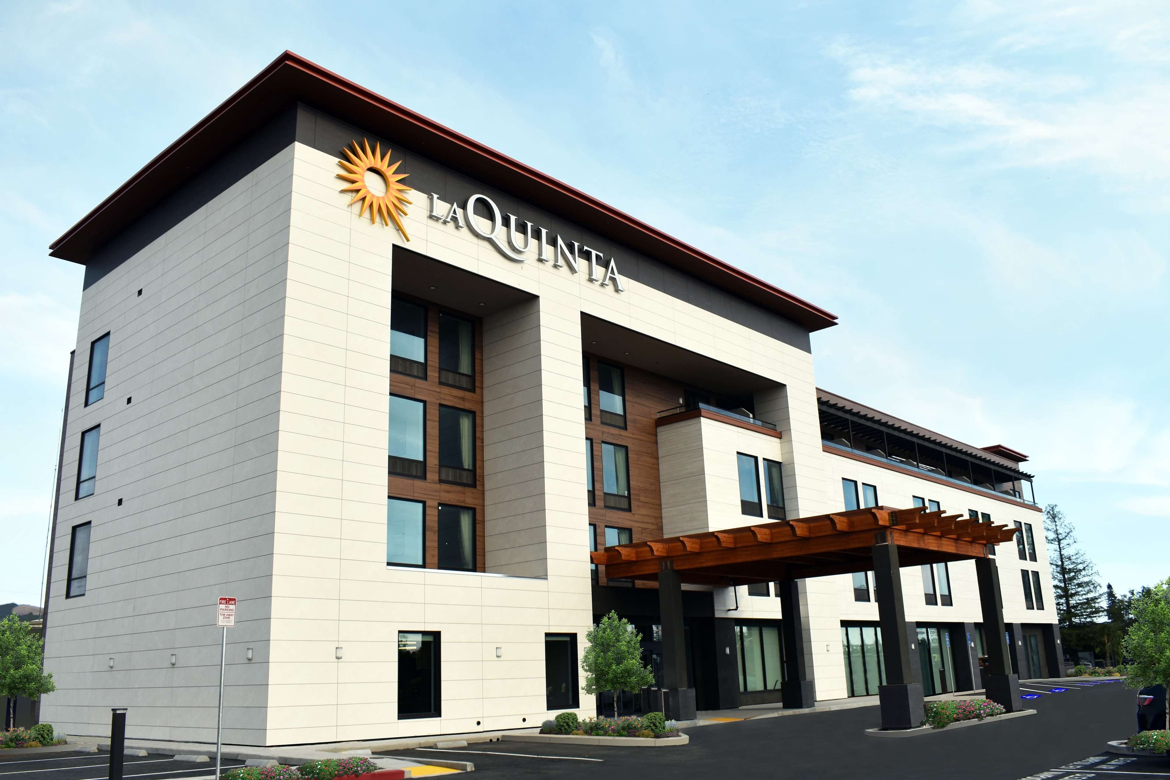 A La Quinta hotel with a modern design, featuring a prominent sun logo, a covered entrance, and a parking area.