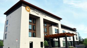 A La Quinta hotel with a modern design, featuring a prominent sun logo, a covered entrance, and a parking area.