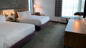 A hotel room with two beds, a desk, a chair, a lamp, and a window with curtains.