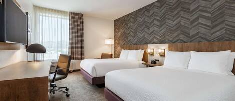 Quarto de hotel com duas camas, uma escrivaninha, uma cadeira e uma televisão.