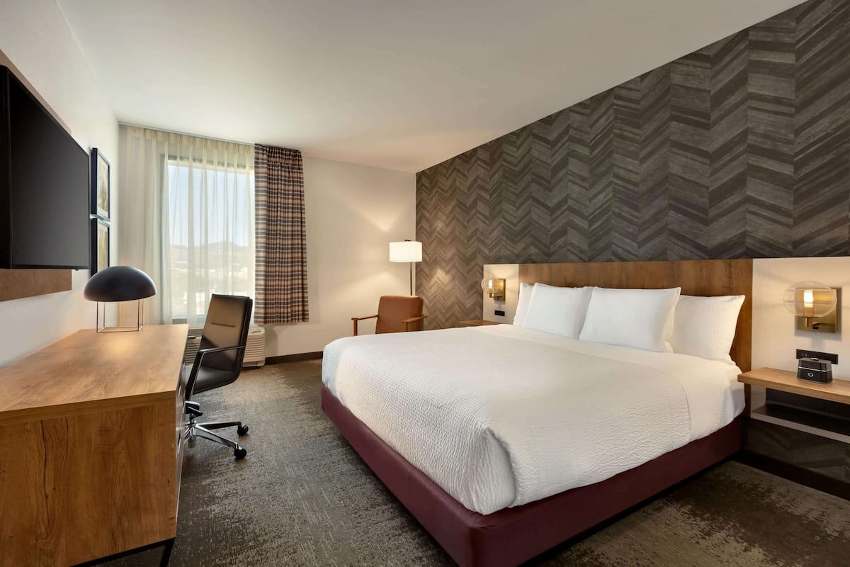 A hotel room with a large bed, a desk, a chair, a TV, and a window with curtains.