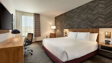 A hotel room with a large bed, a desk, a chair, a TV, and a window with curtains.