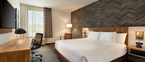 A hotel room with a large bed, a desk, a chair, a TV, and a window with curtains.