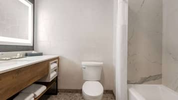 Et badeværelse med et hvidt toilet, en trækommode med spejl og et badekar.