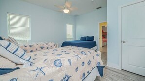 Un dormitorio con dos camas, un ventilador de techo y una puerta que da a otra habitación.