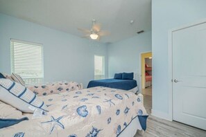 Un dormitorio con dos camas, un ventilador de techo y una puerta que da a otra habitación.