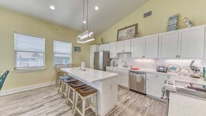 Una cocina con una isla central, taburetes de bar, un refrigerador, un lavavajillas y un lavamanos.