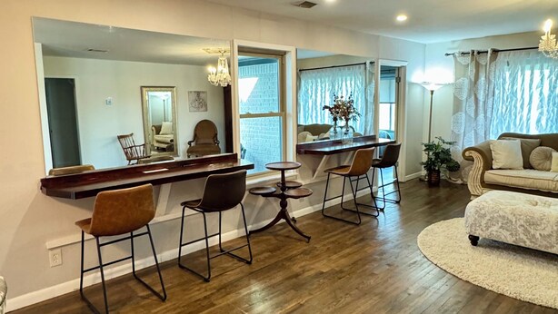 Una sala de estar amplia con pisos de madera, un comedor con mesa y sillas de madera, un espejo grande y una zona de estar acogedora con un sofá y un tapete redondo.