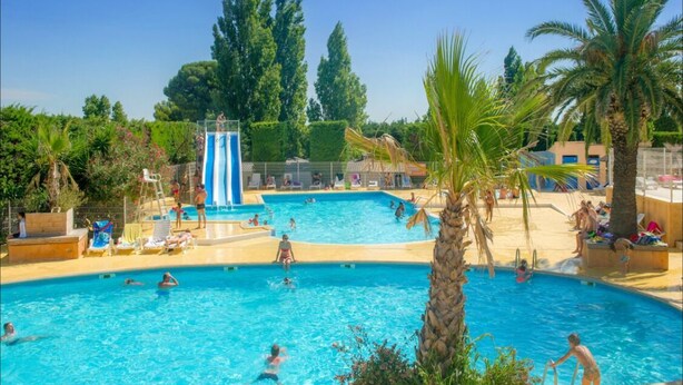 Zona de piscina con varias piscinas, palmeras y un tobogán.