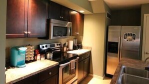 A compact kitchen with dark wood cabinets, a stainless steel microwave, a built-in oven, and a refrigerator. - Athens townhouse, 4 beds, 2 kings. 2 twins, in 2 bedrooms, 2,5 baths, FREE WIFI, (Athens)