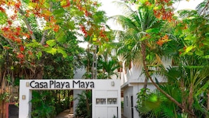 A gated entrance to Casa Playa Maya with a white signboard, surrounded by lush tropical vegetation.