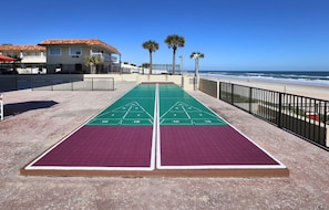 A shuffleboard table with a clear view of the ocean and beach in the background.