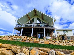 A two-story house with a stone foundation, a covered porch, and a balcony. - Golf Course Lakehouse with fantastic views of the lake, mountains & golf course. (Garden City)