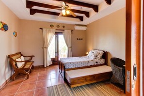 A bedroom with a bed, a chair, a ceiling fan, and a window with curtains. - Oceanview Villa w/ private pool, beachside access in Rancho Santana!  (El Limón)