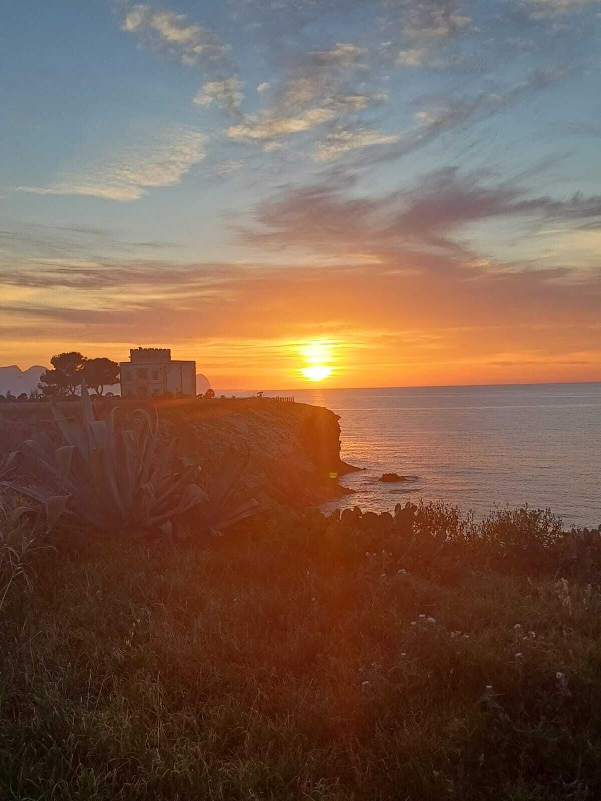 Una puesta de sol costera con un edificio en un acantilado con vista al mar.