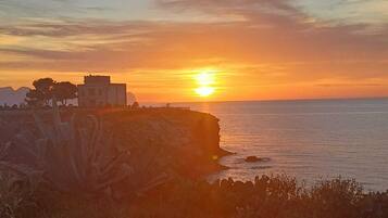 Una puesta de sol costera con un edificio en un acantilado con vista al mar.