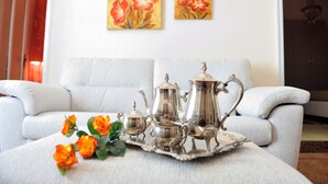 A living room with a white sofa, a tray with silver tea set, and orange roses on a table.