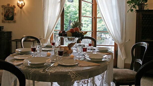 A dining table set for four with plates, glasses, and cutlery. A fruit bowl is on the table, and there is a window with curtains. - Residenza Oltrarno, an elegant apartment in the historic center of Florence (Firenze)