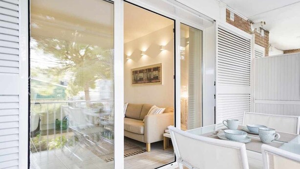 Un espace repas extérieur moderne, avec une table et des chaises en verre, un canapé et un tableau accroché au mur.