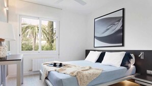 Une chambre moderne avec un lit, une table de chevet et une fenêtre donnant sur des palmiers.