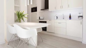 Une cuisine moderne avec des meubles blancs, une table à manger blanche accompagnée de deux chaises, un four à micro-ondes, un grille-pain et une machine à café.