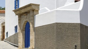 Un edificio blanco con puerta y ventanas azules, un arco de piedra y cielo despejado.