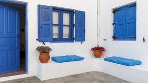 Un edificio blanco con puertas y contraventanas azules, dos macetas y un banco.