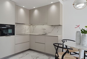 A modern kitchen with built-in appliances, a marble backsplash, and a dining area with a table and chairs.