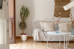 Un soggiorno con un divano, un tavolino bianco rotondo, una pianta in vaso e un elemento decorativo a parete.