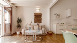 A modern living room with a sofa, two round tables, a potted plant, and a kitchen area with cabinets and a countertop. -  DOMUS DE SILVA - Apartment in the historic center of Cagliari (Cagliari)