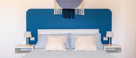 A bed with a blue headboard, two bedside tables with lamps, and a hanging macrame piece above the bed.