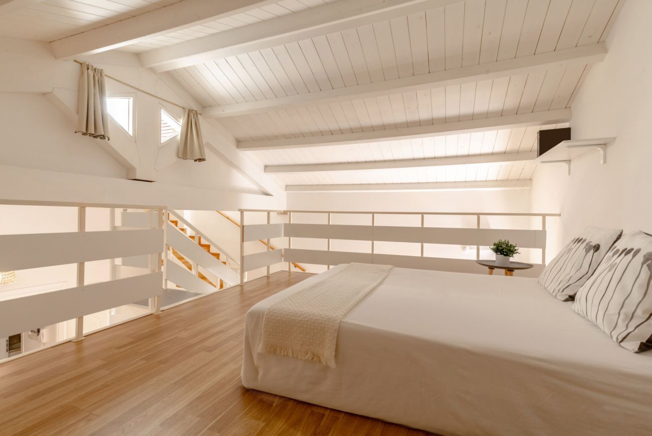 Un dormitorio con una cama grande, suelo de madera, techo blanco y una escalera que sube a un nivel superior.