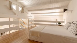 A bedroom with a large bed, wooden flooring, a white ceiling, and a staircase leading to an upper level. -  DOMUS DE SILVA - Apartment in the historic center of Cagliari (Cagliari)
