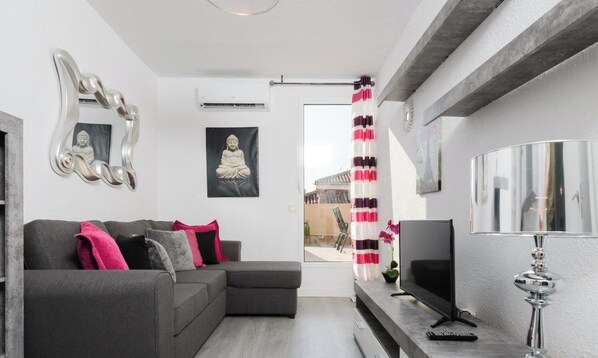 A modern living room with a grey sofa, a TV, a decorative mirror, and a Buddha statue.