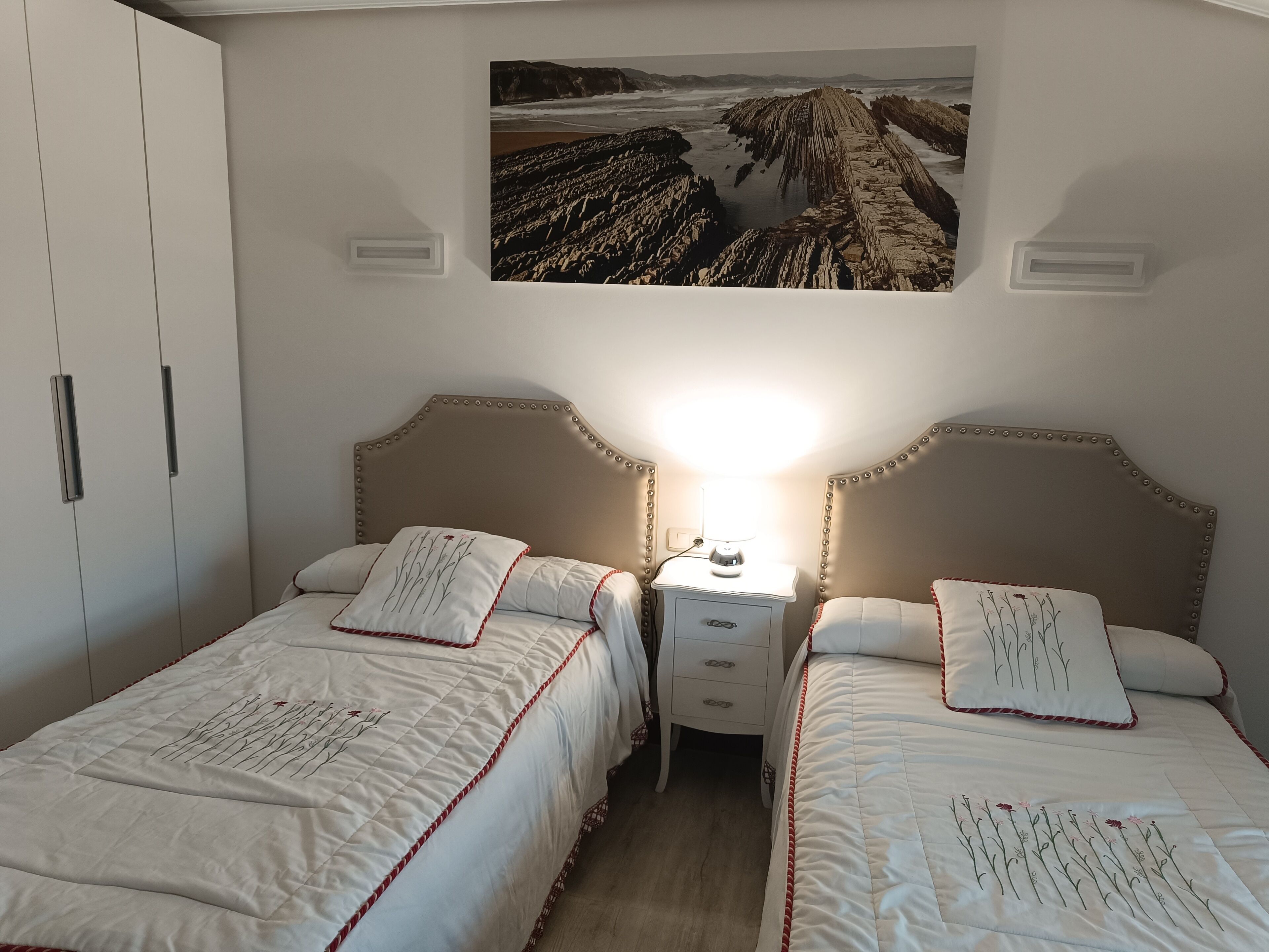 Een slaapkamer met twee enkele bedden, een nachtkastje met een lamp en een groot, ingelijst schilderij aan de muur.
