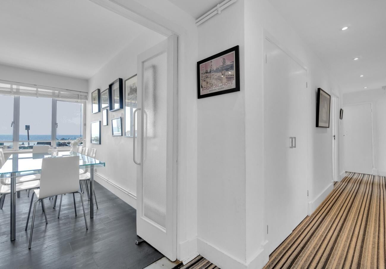 A modern hotel corridor with a dining area, framed pictures on the walls, and a view of the sea.