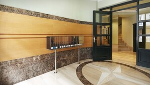 Um lobby de hotel com piso de mármore, balcão de recepção de madeira e porta de vidro que dá para uma escadaria.