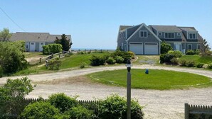 A residential area with a large house featuring a garage, a well-maintained lawn, and a clear view of the ocean.