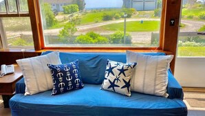 A blue sofa with patterned pillows, a wooden window frame, and a view of a residential area.