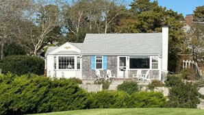 A white building with blue shutters, a porch, and a chimney.