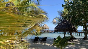 Una playa con sillas de descanso, palmeras y una estructura de techo de paja sobre el agua.