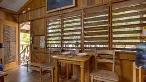 Un comedor de madera con una mesa, sillas, un dispensador de agua y vistas a través de persianas de bambú.