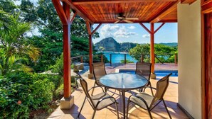 A covered outdoor area with a pool, surrounded by lush greenery and a mountainous backdrop. - Oceanfront treehouse home w/ private pool, deck, near beach (Tola)